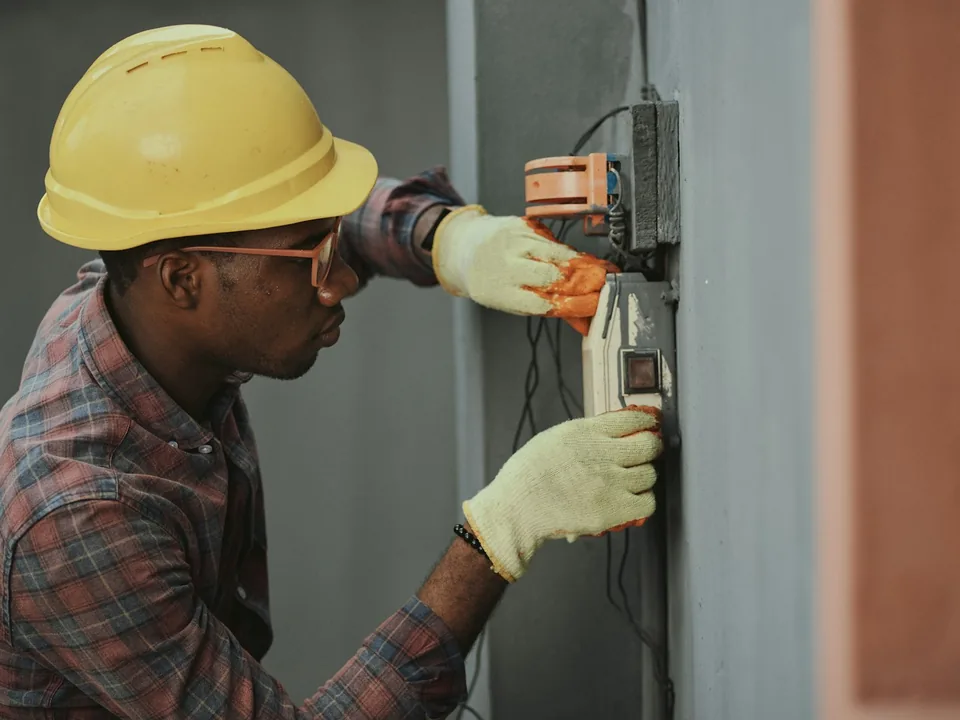 Technicien frigoriste au travail sur une armoire électrique, casque et gants isolants